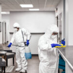 Two people in protective workwear cleaning and disinfecting offices.